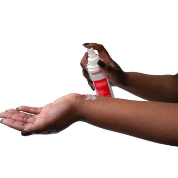 Persoon spuit lotion op arm voor hydratatie.