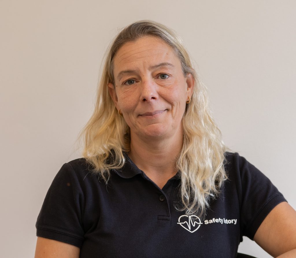 Vrouw in blauwe polo met logo, kijkt naar camera.