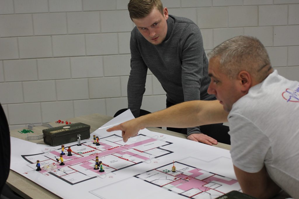 Mannen bespreken plattegrond met speelgoedsoldaatjes.